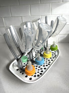 Baby bottle drying rack with an assortment of Sepal  bottles, teats and caps on the rack. Sitting on a kitchen bench.