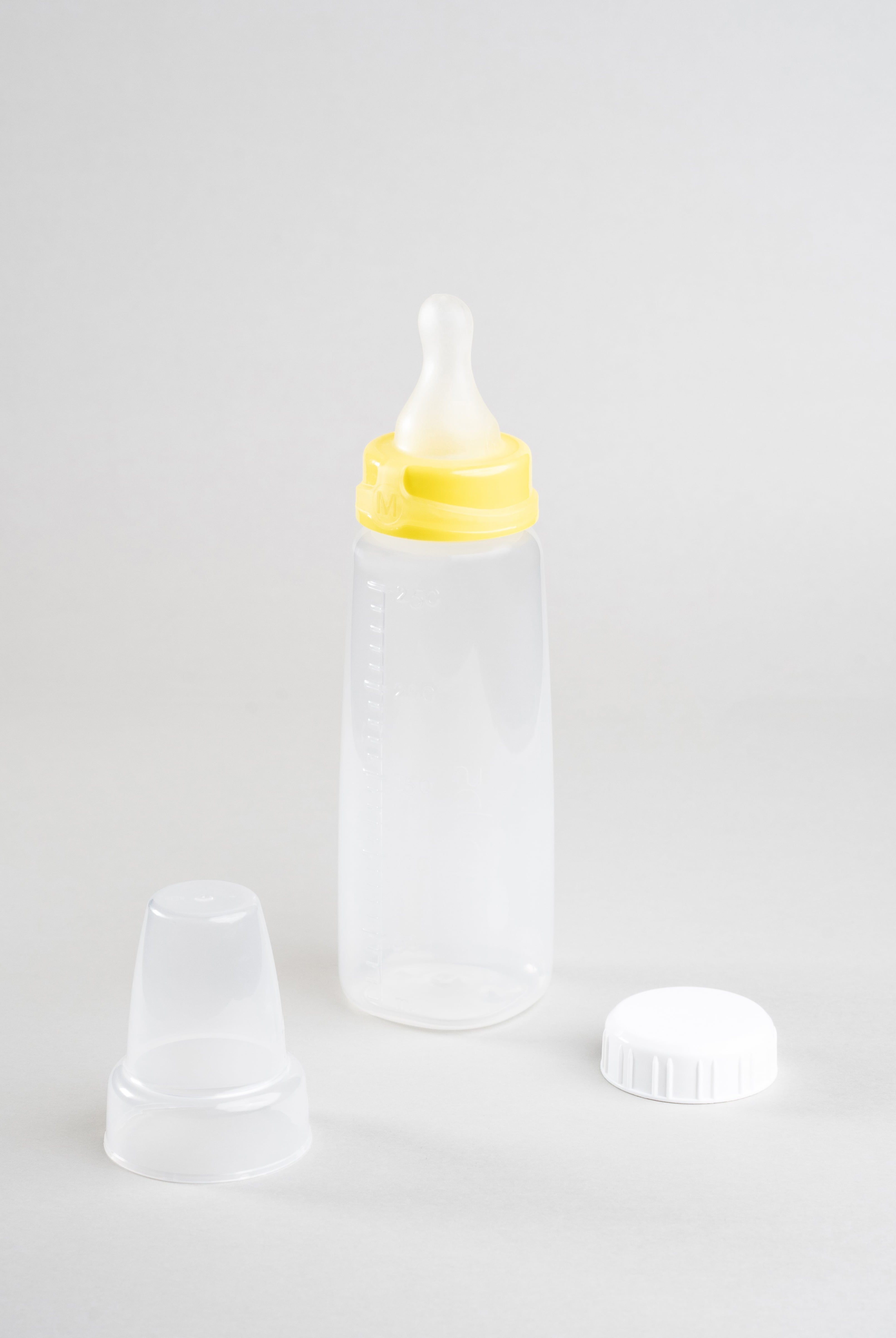 Sepal 250ml baby bottle with yellow medium teat medium flow attached. Beside the bottle is a white Sepal bottle cap and clear Sepal teat cover.