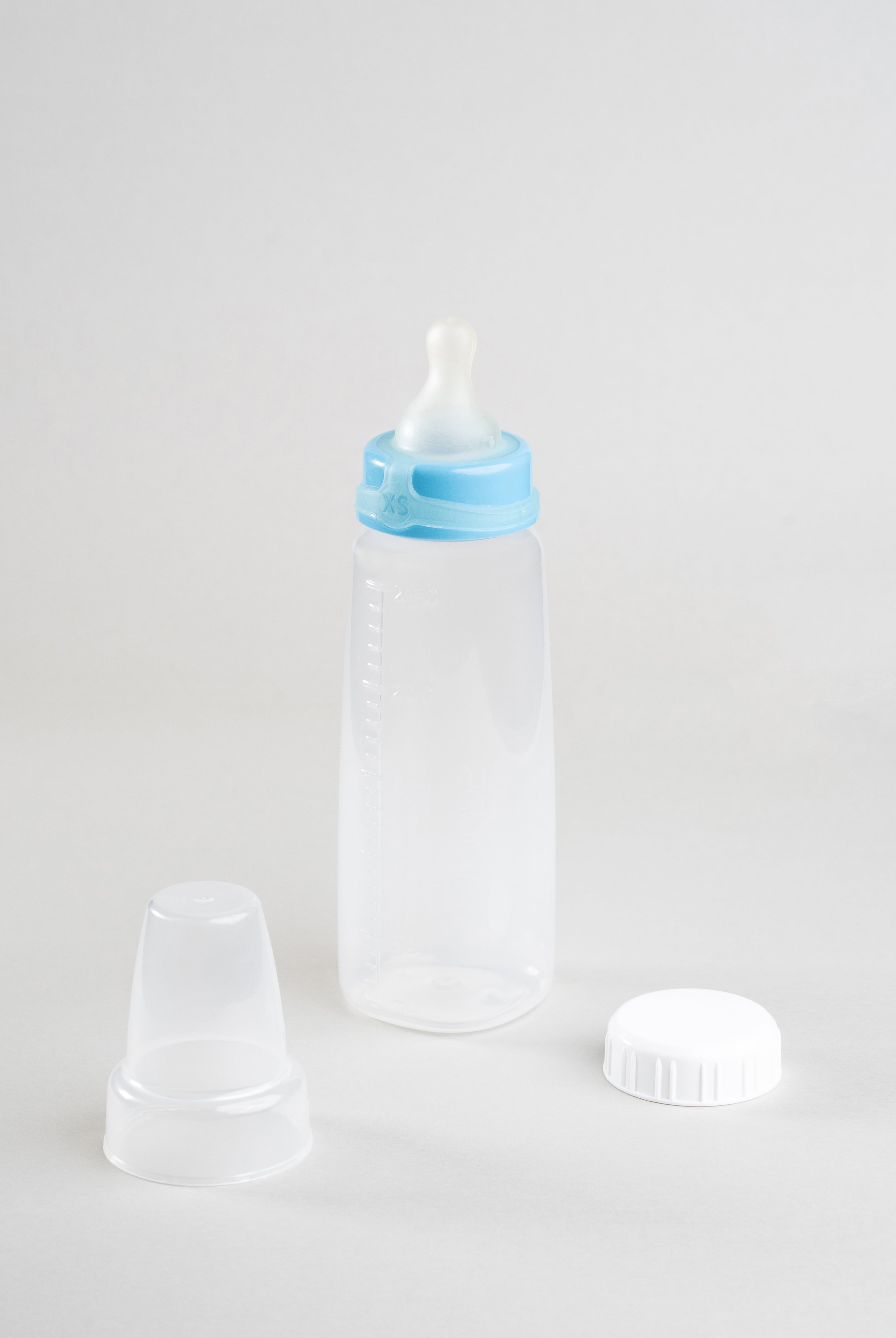 Sepal 250ml baby bottle with blue extra small extra slow flow teat attached. Beside the bottle is a Sepal white cap and a clear Sepal teat cover.