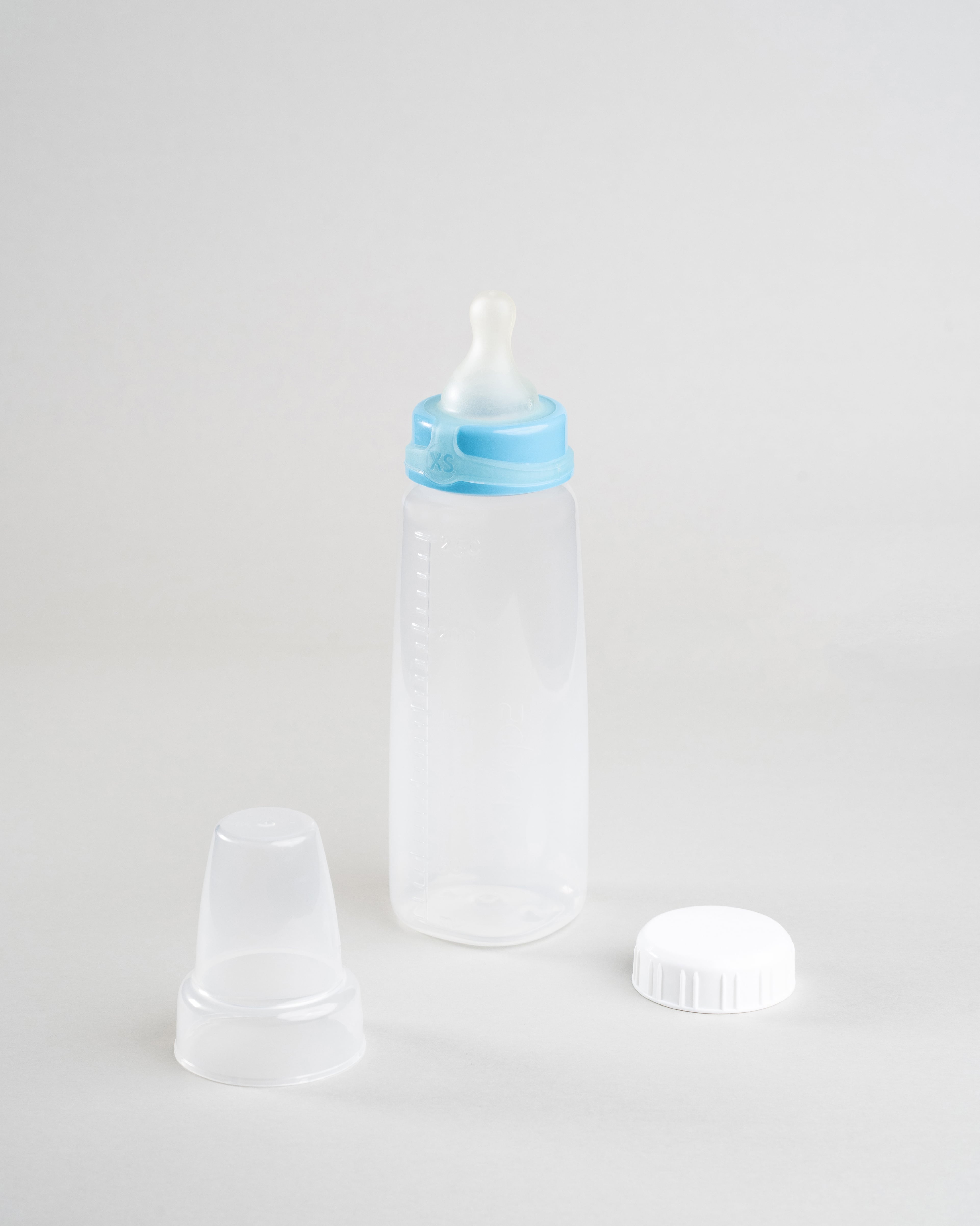 Sepal 250ml baby bottle with blue extra small extra slow flow teat attached. Beside the bottle is a Sepal white cap and a clear Sepal teat cover.