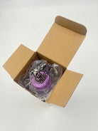 A packaged purple baby teat inside an open brown cardboard box on a plain white background.